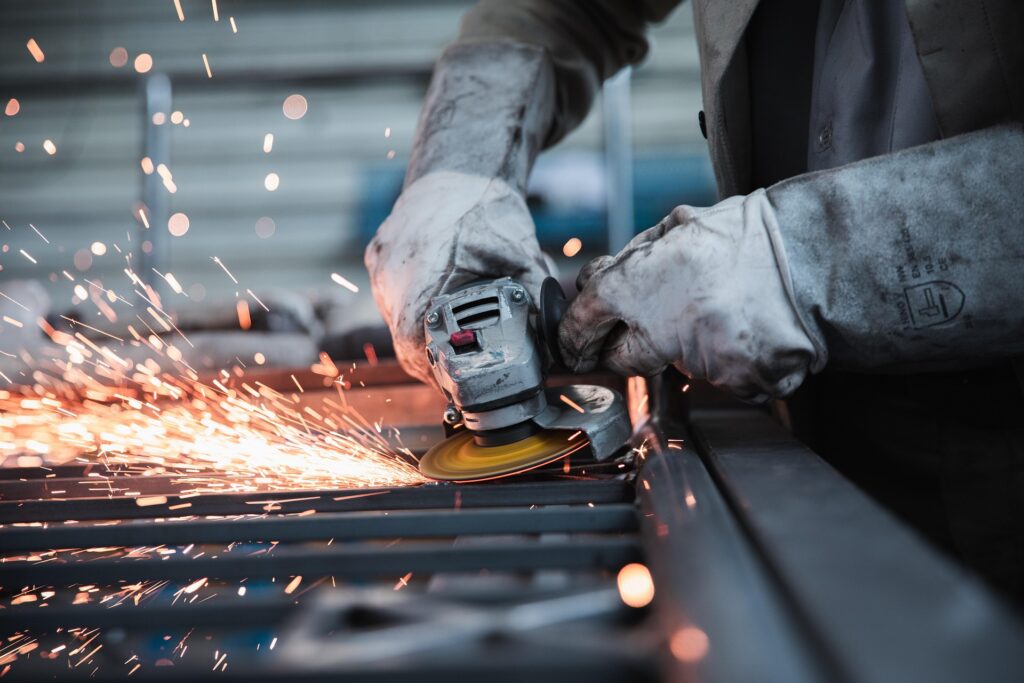 Industrial worker grinding metal components inside a manufacturing facility with sparks during fabrication.