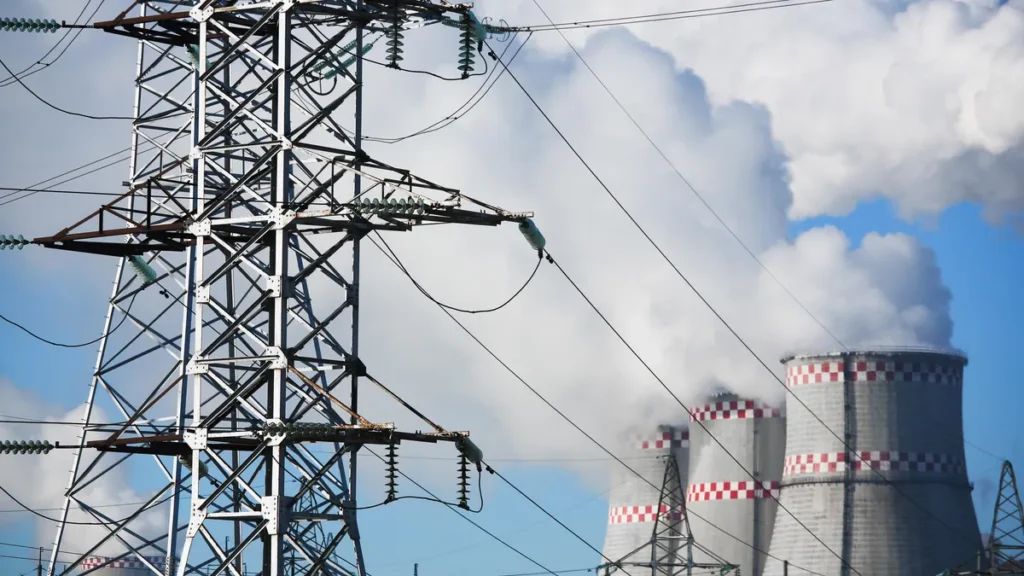 High-voltage power transmission tower near electrical power generation facility with industrial energy infrastructure.